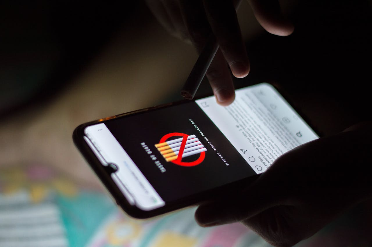 A person browsing social media on a smartphone at night, holding a cigarette.